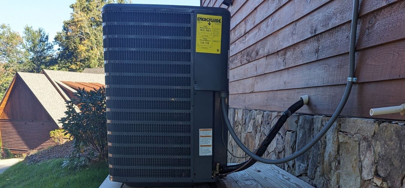 Outdoor air conditioning unit installed on a wooden platform next to a house with stone siding and wood paneling by a trusted air conditioning contractor Hickory NC.