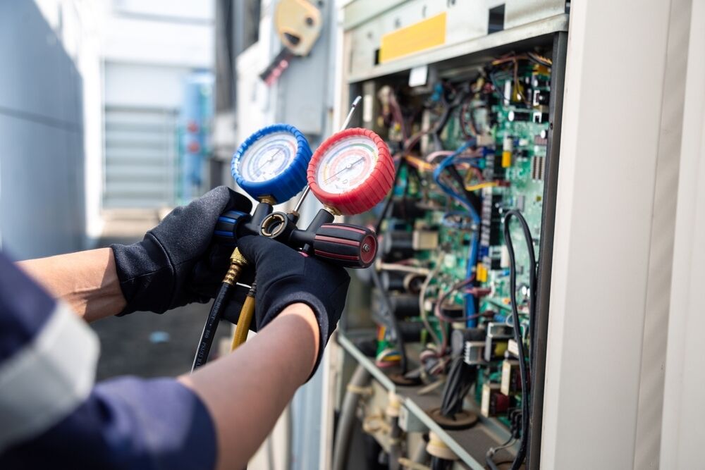 Technician using pressure gauges to check an air conditioning unit outside.