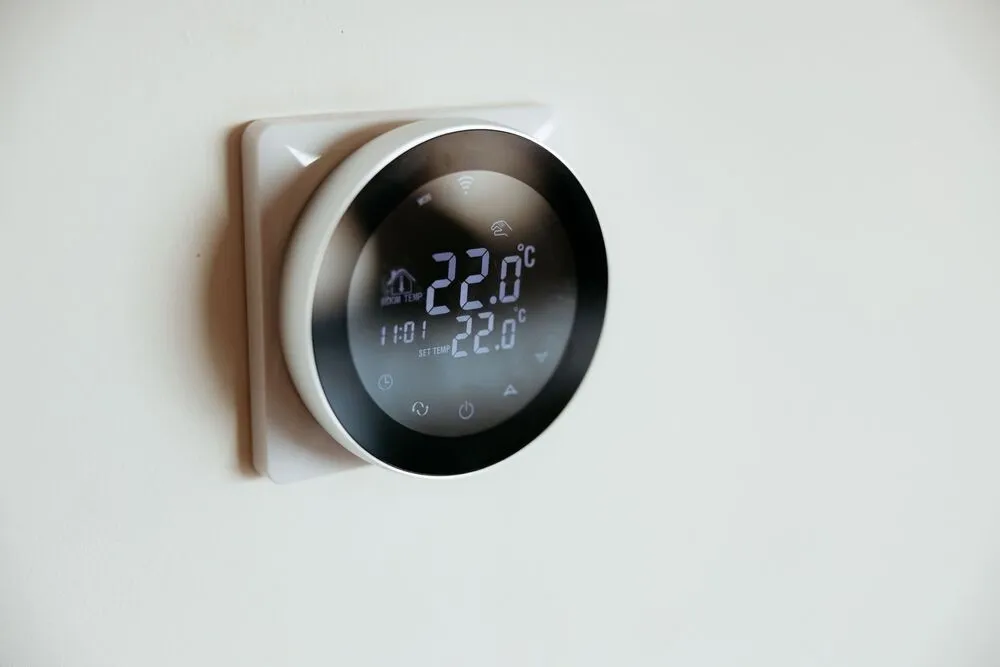 A digital thermostat is mounted on a wall, displaying a temperature of 22 degrees Celsius.