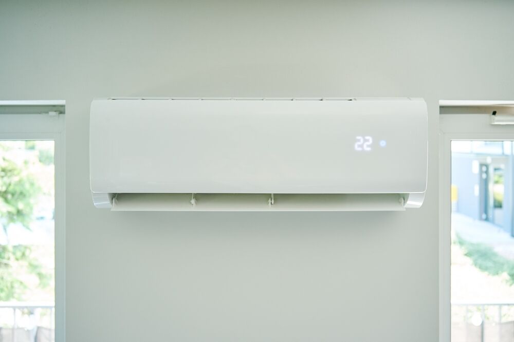 Wall-mounted air conditioning unit with digital display showing 22 degrees. Two windows are partially visible on either side.