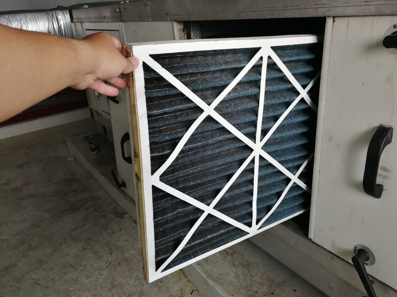 A person is removing a dirty air filter from an HVAC unit for replacement or cleaning.