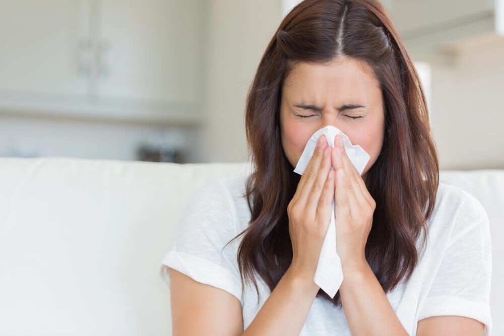 Woman blowing her nose with a tissue, emphasizing the importance of furnace repair for healthy living.