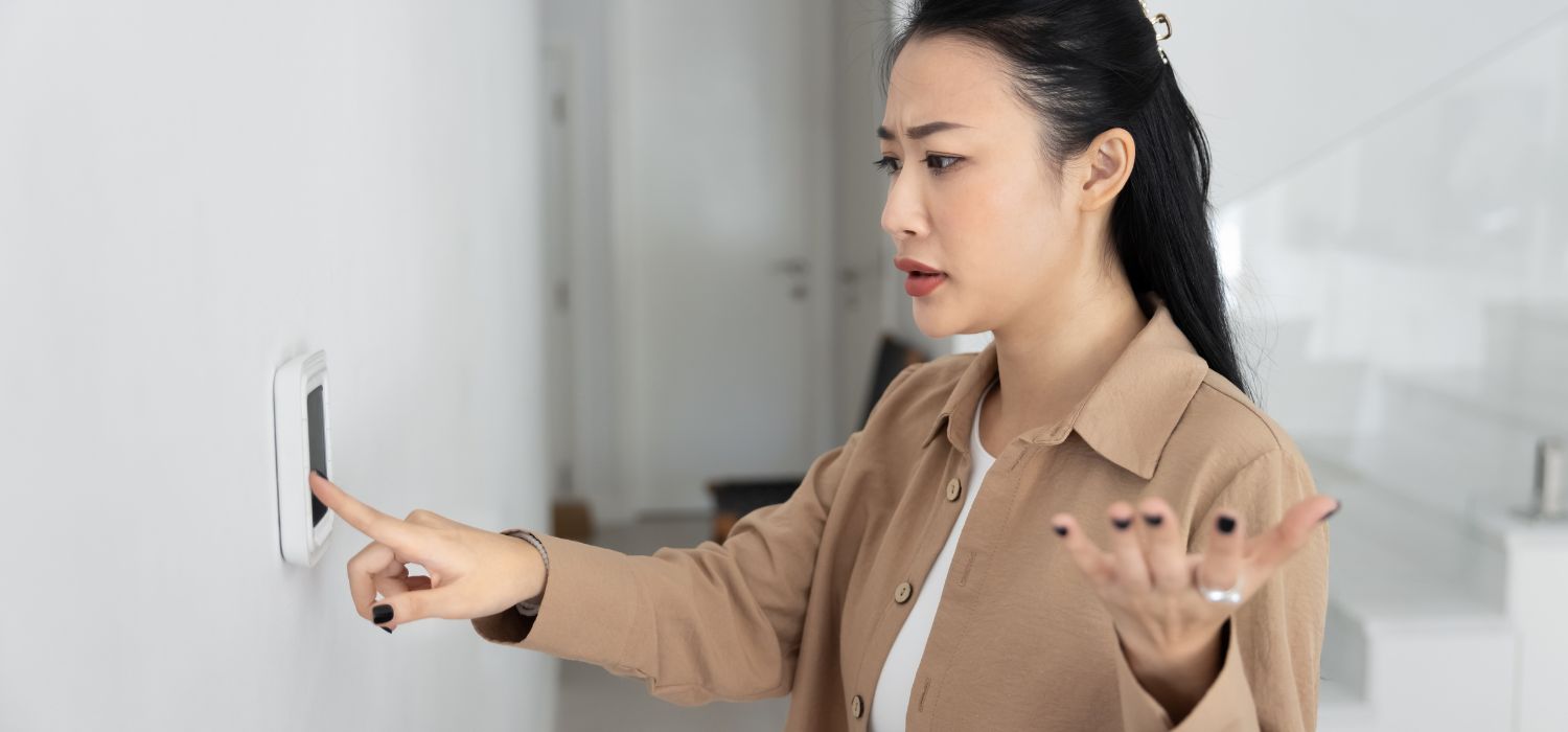 Frustrated homeowner adjusting a wall thermostat while dealing with uneven indoor temperatures and airflow issues.