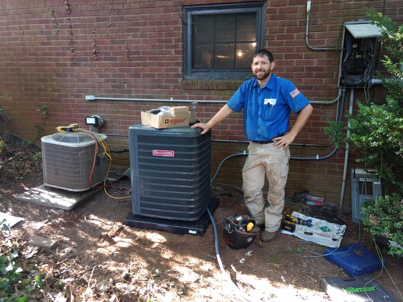 Hvac technician standing next to a newly installed air conditioning unit outside a brick home in Hickory NC