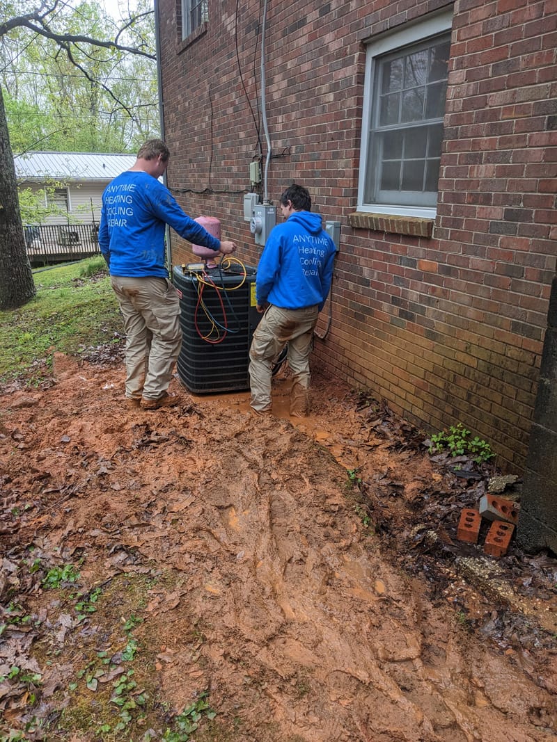 Two men working on ac unit behind house.