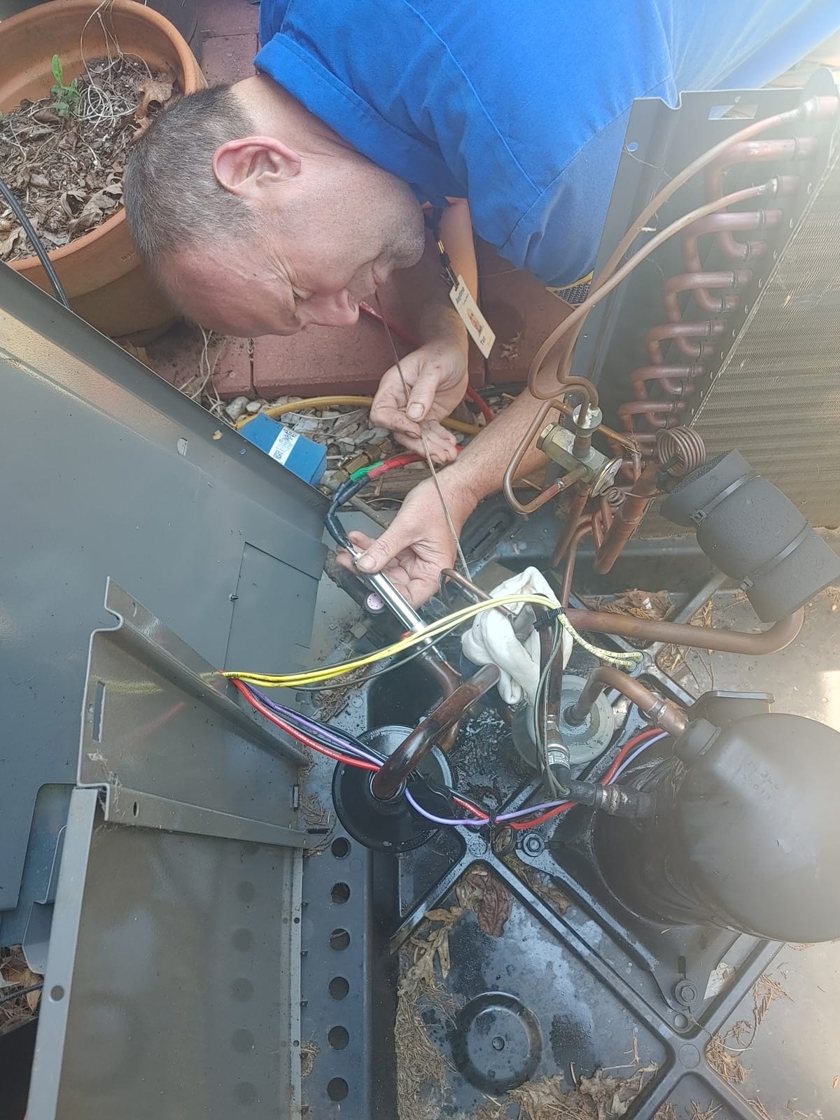 A technician is repairing internal components of an air conditioning unit outdoors.