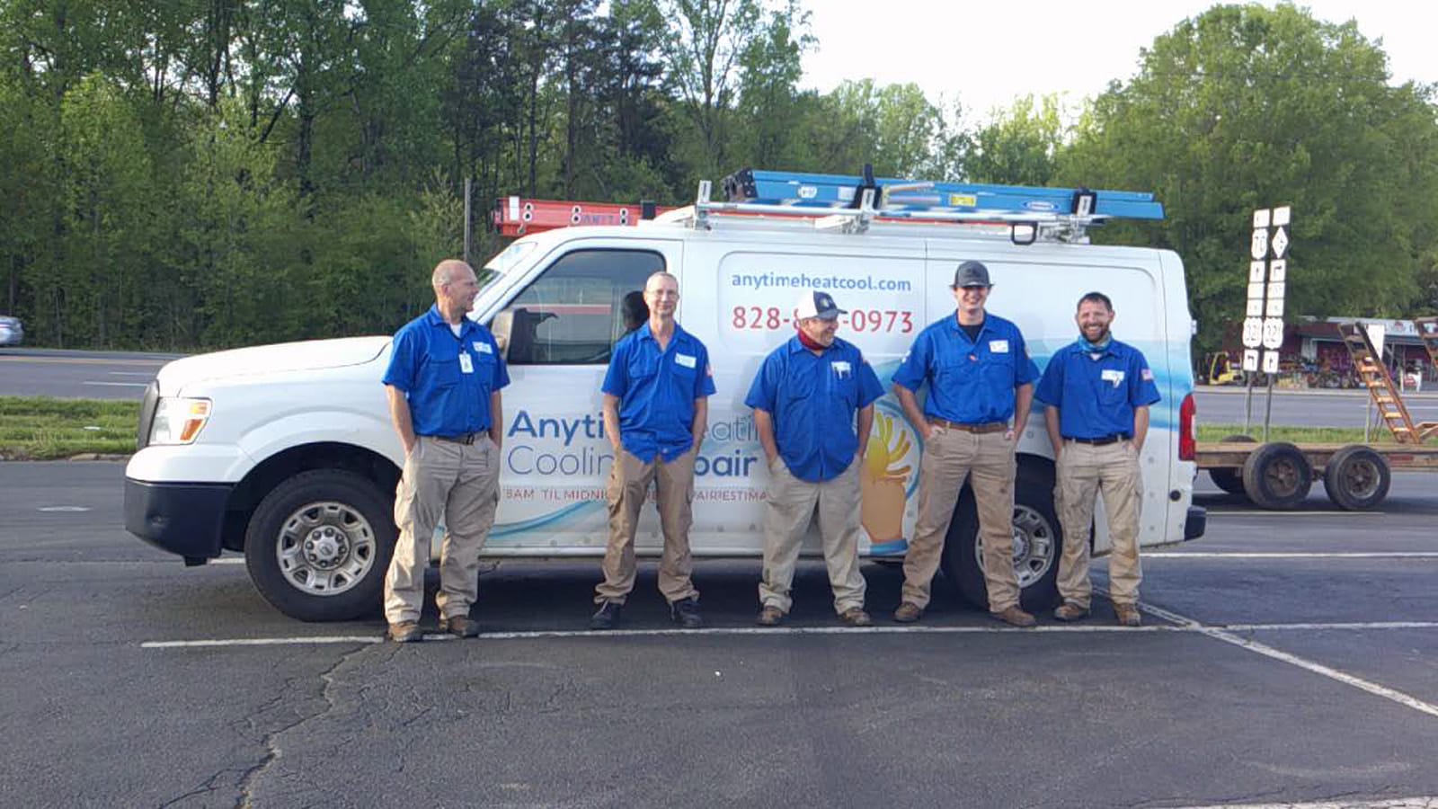 Five technicians in uniforms standing in front of their company van, equipped with ladders and HVAC repair equipment
