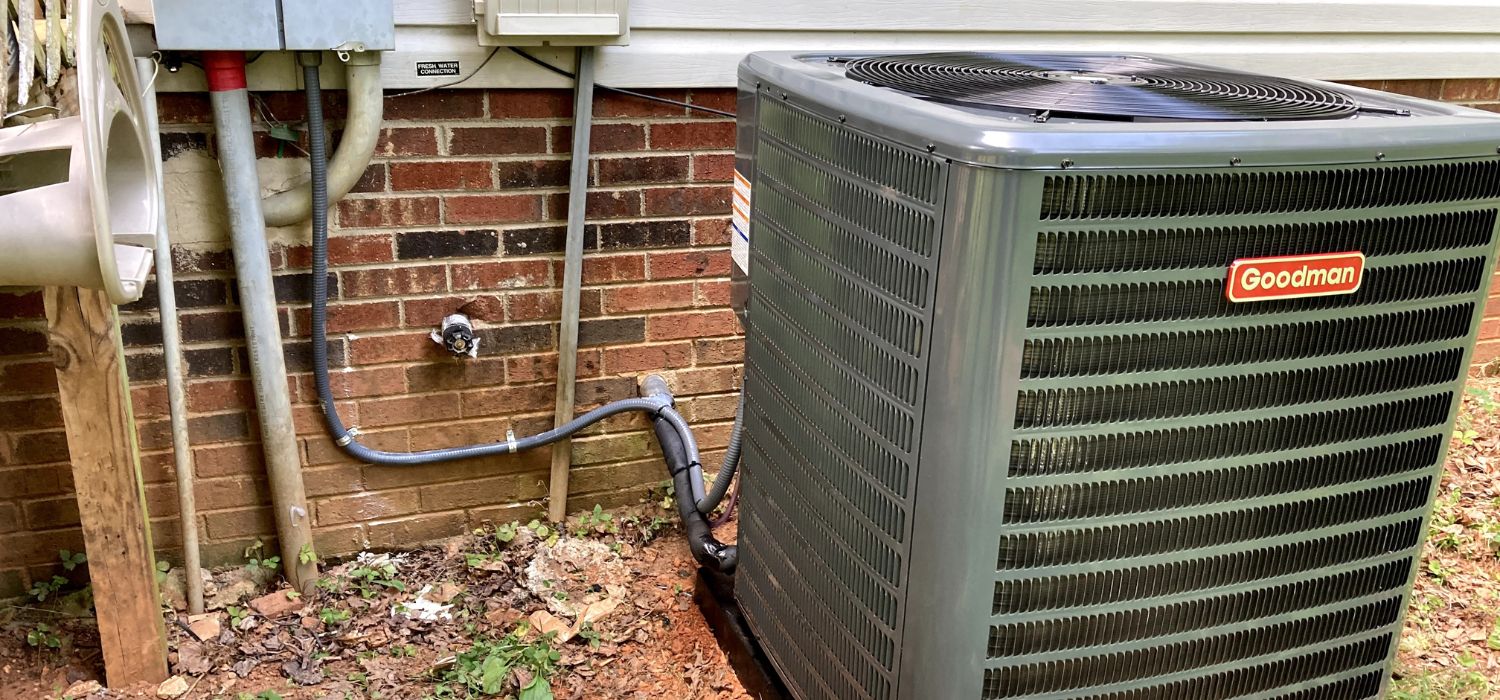 Outdoor Goodman air conditioning condenser installed next to a brick home, showing the exterior HVAC unit and connected utility lines.