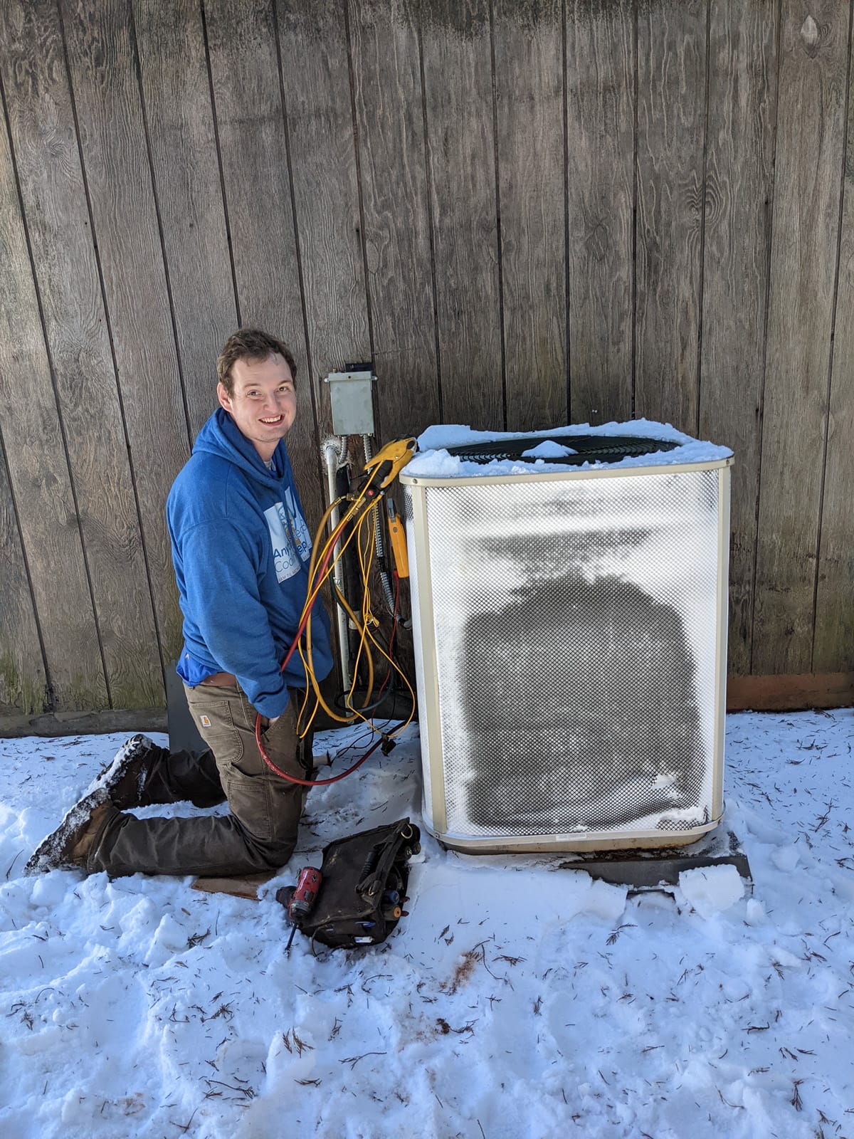 Technician employing HVAC leak detection methods while servicing an outdoor air conditioning unit in winter conditions.