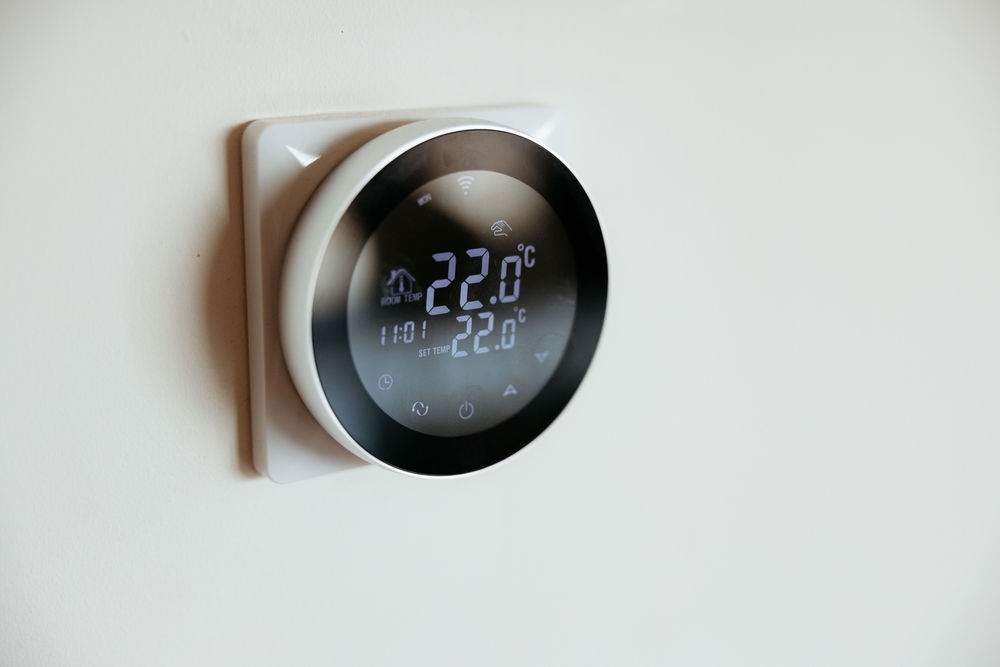 A digital thermostat is mounted on a wall, displaying a temperature of 22 degrees Celsius.