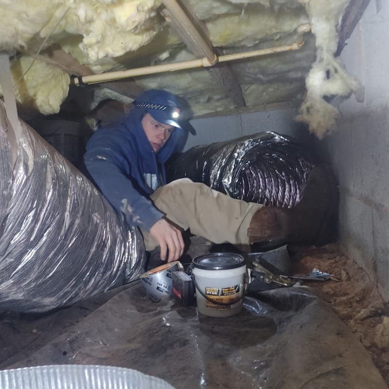 A person working on air ducts in a cramped crawl space.